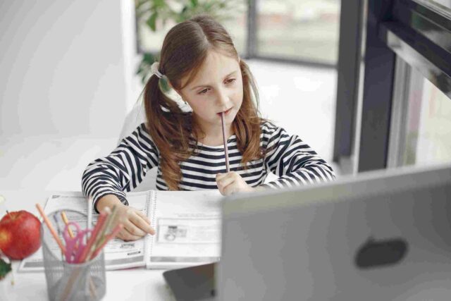 A young student looking thoughtfully at a laptop and notebook.