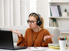 Can I Ask Someone to Take My Online Exam For Me? A confused student with headphones and glasses looking at a laptop. Ideal for "take my online exam for me" academic services.