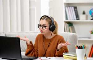 Can I Ask Someone to Take My Online Exam For Me? A confused student with headphones and glasses looking at a laptop. Ideal for "take my online exam for me" academic services.