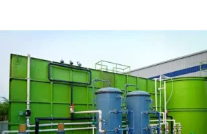 What is an STP Plant and How It Works in Modern Wastewater Treatment Industrial water treatment system with large green tanks, blue filtration vessels, and interconnected pipes and pumps outdoors.